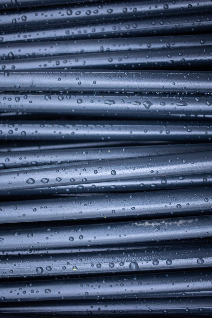 Abstract textured backdrop of full frame dark rubber rods with drops on shiny surface